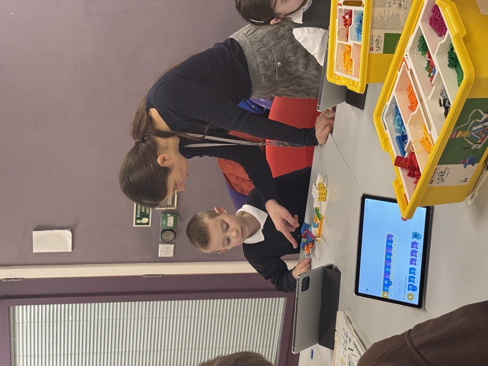 A facilitator helping a child follow a build on a tablet during a session.