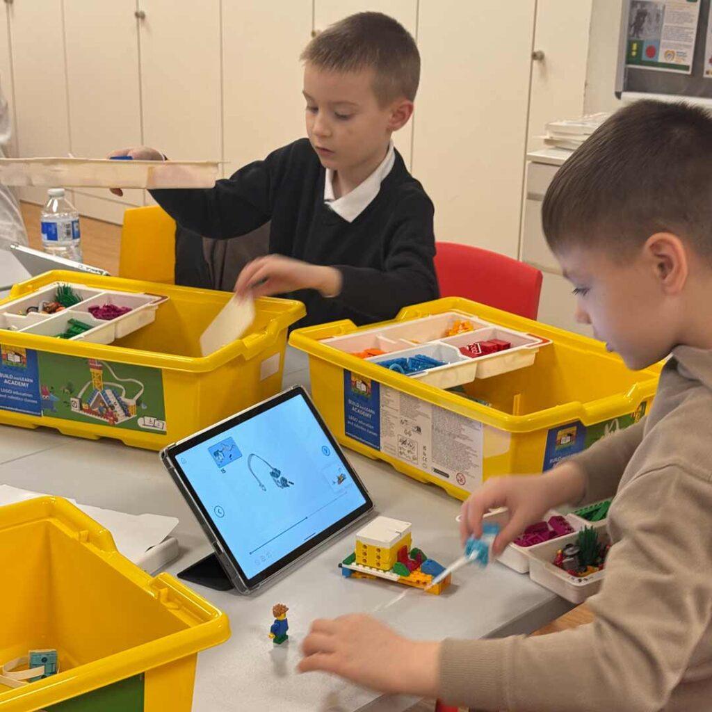 Two children working together on a building task with a tablet guide.